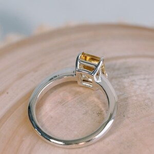 May include: A silver ring with a yellow gemstone set in a square bezel.