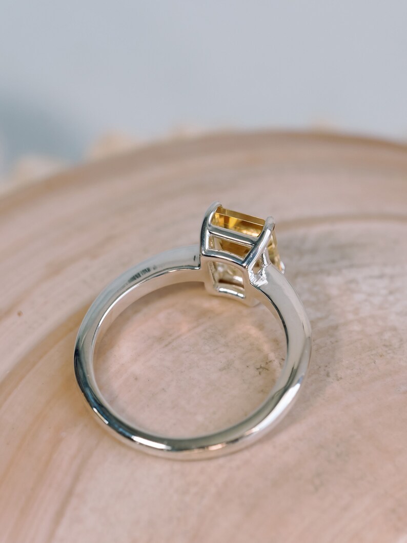 May include: A silver ring with a yellow gemstone set in a square bezel.