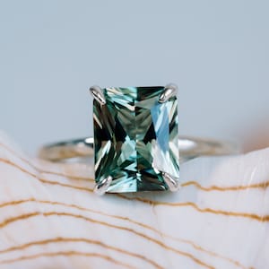 May include: A silver ring featuring a large, emerald-cut green gemstone.