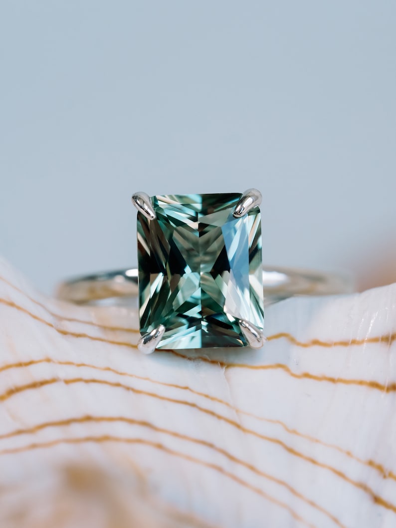 May include: A silver ring featuring a large, emerald-cut green gemstone.