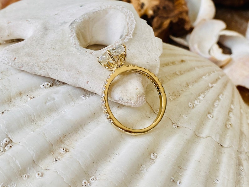Pode incluir: Um anel de noivado de ouro com uma grande pedra de diamante redonda e clara no centro e uma banda de diamantes menores.