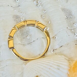 May include: A gold band ring with a unique design featuring a series of rectangular shapes. The ring is set against a white background.