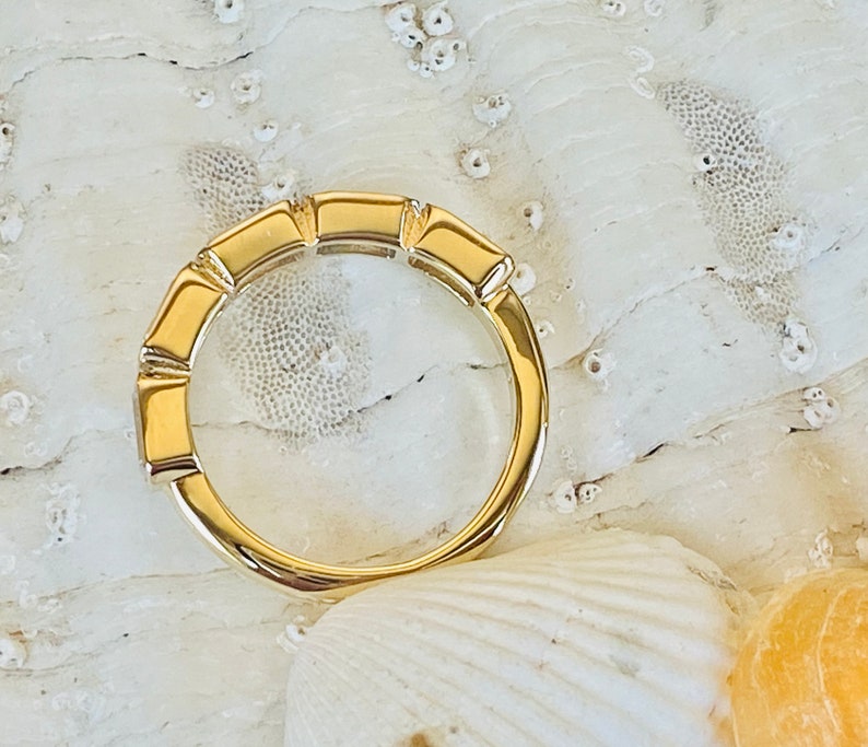 May include: A gold band ring with a unique design featuring a series of rectangular shapes. The ring is set against a white background.