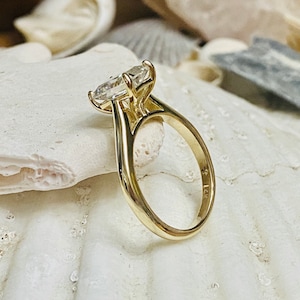 May include: A gold engagement ring featuring a large, clear, oval-shaped diamond. The ring is set on a simple band and has a size 7 inscription on the inside.