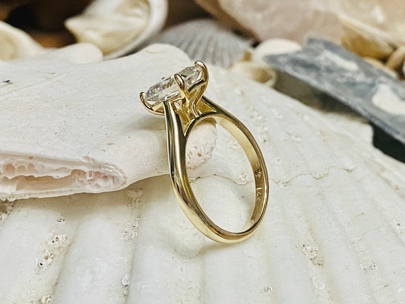 May include: A gold engagement ring featuring a large, clear, oval-shaped diamond. The ring is set on a simple band and has a size 7 inscription on the inside.