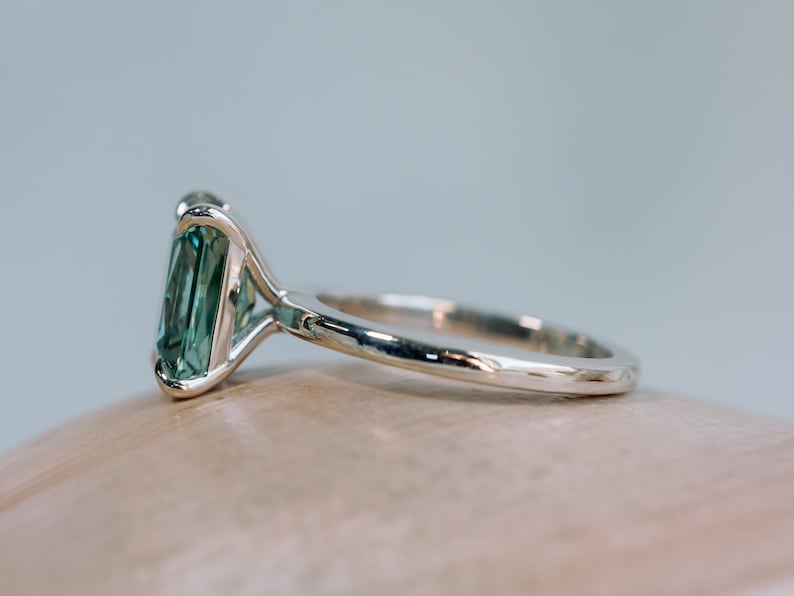 May include: A silver ring featuring a large, emerald-cut green gemstone set in a prong setting.