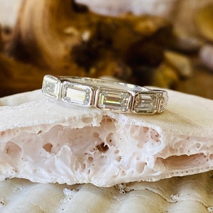 May include: A silver band ring with a row of emerald-cut diamonds.