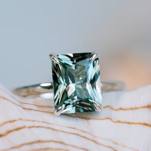 May include: A silver ring featuring a large, emerald-green gemstone set in a square shape.