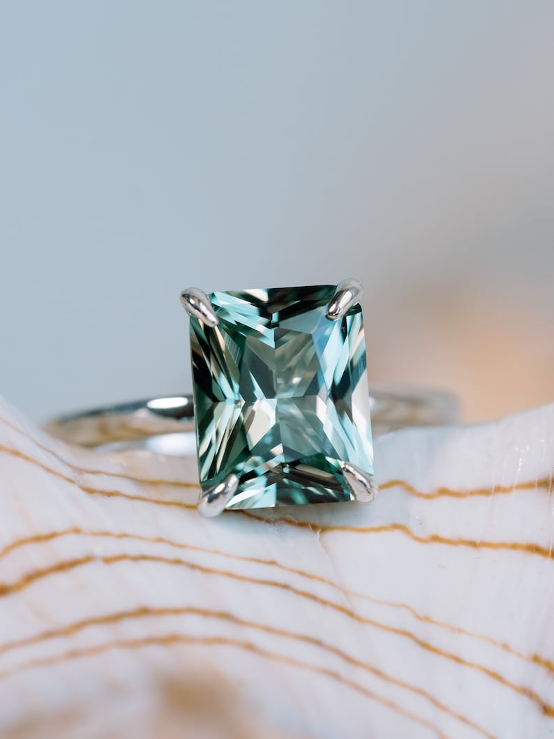 May include: A silver ring featuring a large, emerald-green gemstone set in a square shape.