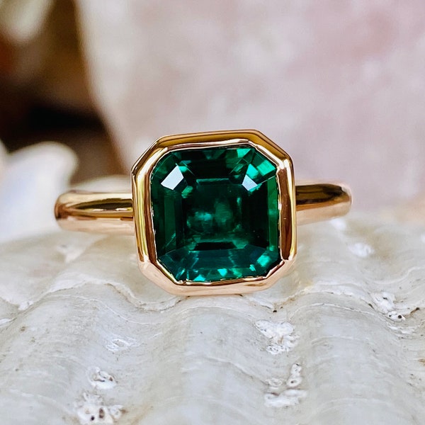 May include: A gold ring with a large, emerald green gemstone set in a square bezel.