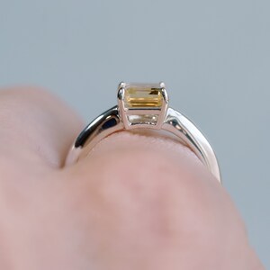 May include: A silver ring with a rectangular, light yellow gemstone.