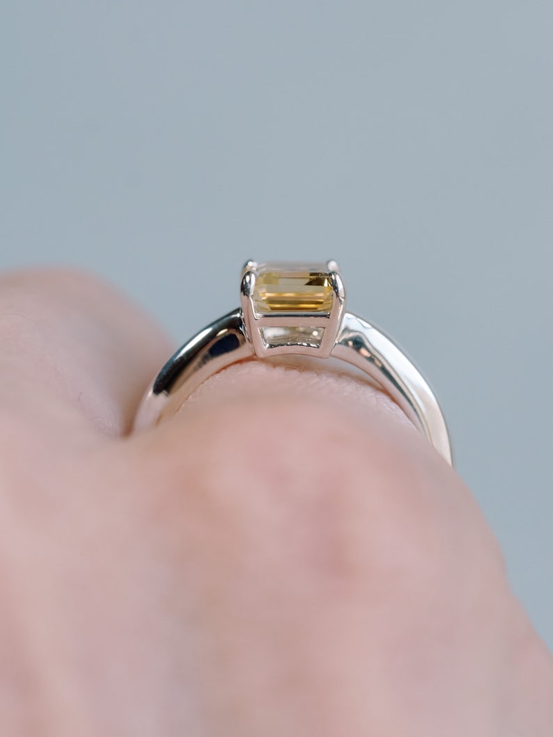 May include: A silver ring with a rectangular, light yellow gemstone.