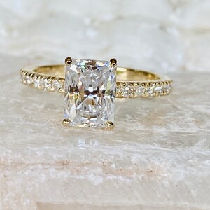 Pode incluir: Um anel de noivado de ouro com uma grande pedra central de diamante retangular e transparente, e uma banda de diamantes menores.