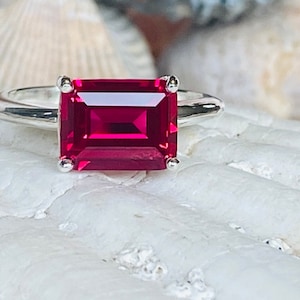 Puede incluir: Un anillo de plata con una gran piedra preciosa de rubí rojo oscuro rectangular.