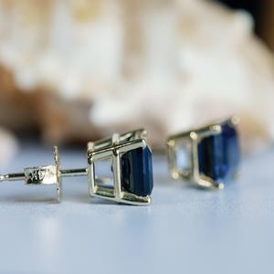 Puede incluir: Un par de pendientes de oro con piedras preciosas de color azul oscuro. Los pendientes tienen un dise&ntilde;o simple y elegante.