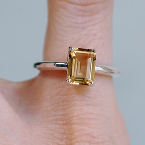 May include: A silver ring with a large, rectangular, light brown gemstone. The gemstone is set in a simple, four-prong setting.