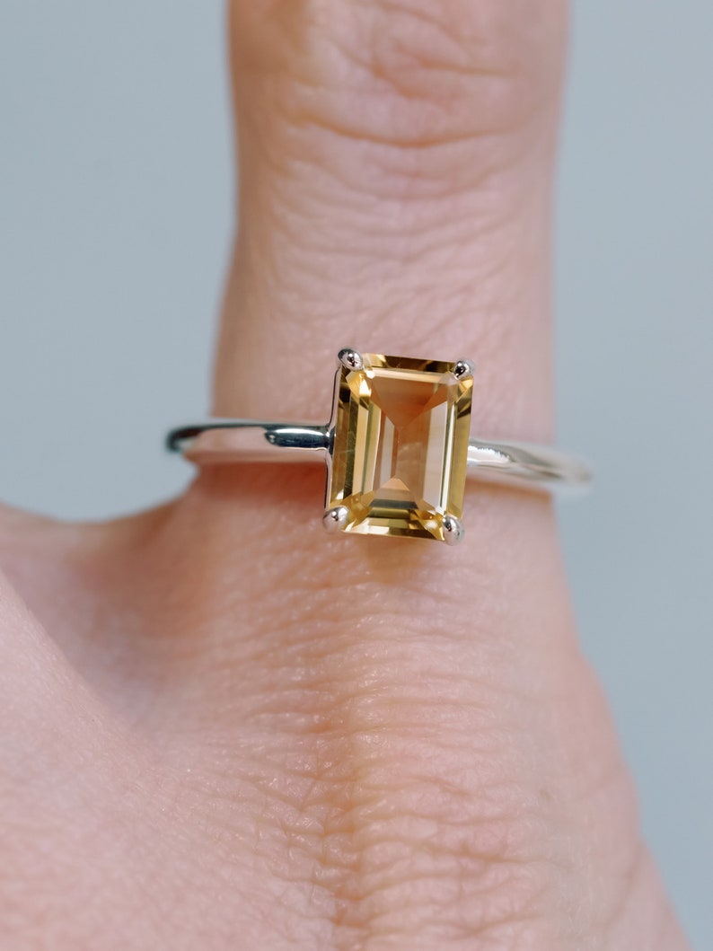 May include: A silver ring with a large, rectangular, light brown gemstone. The gemstone is set in a simple, four-prong setting.