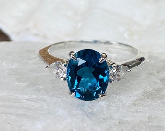 May include: A silver ring with a large oval blue gemstone surrounded by two smaller pear-shaped clear gemstones.
