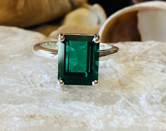 May include: A silver ring with a large emerald green gemstone. The gemstone is cut in an emerald shape.