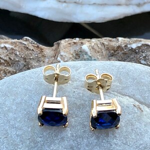 Puede incluir: Un par de pendientes de oro con una piedra preciosa azul oscuro en cada uno. Los pendientes tienen un dise&ntilde;o simple y cl&aacute;sico.