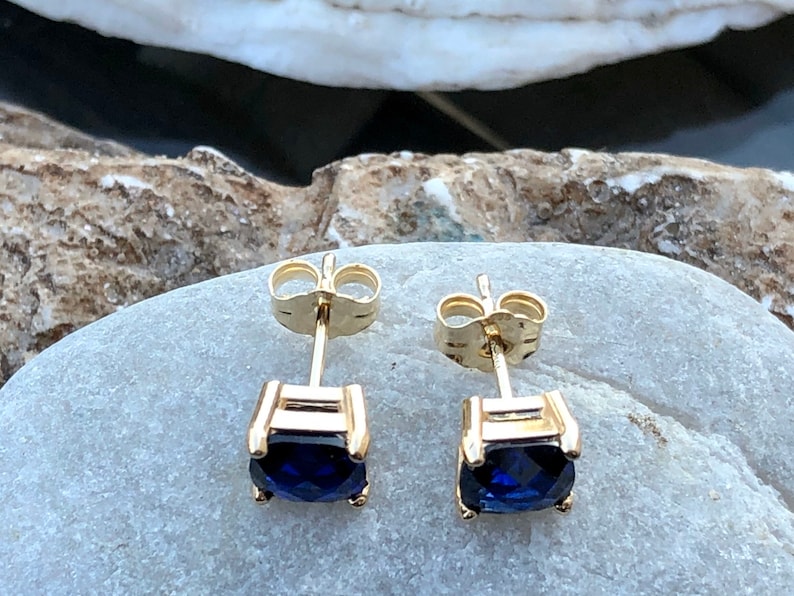 Puede incluir: Un par de pendientes de oro con una piedra preciosa azul oscuro en cada uno. Los pendientes tienen un dise&ntilde;o simple y cl&aacute;sico.