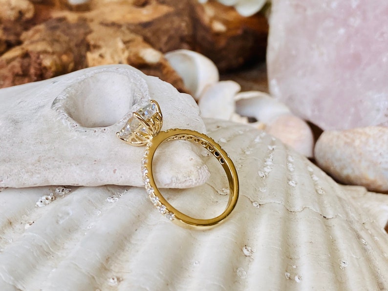 Pode incluir: Um anel de noivado de ouro com uma grande pedra central oval transparente e uma banda de diamantes menores.