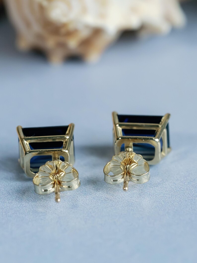Puede incluir: Un par de pendientes de oro con piedras preciosas cuadradas azules. Los pendientes tienen un cierre de poste.