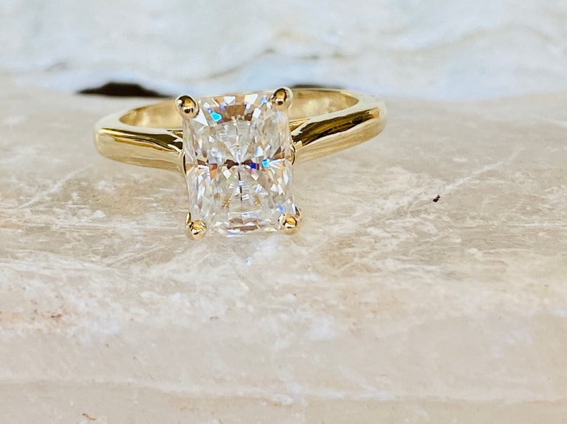 May include: A gold engagement ring featuring a large, clear, rectangular-shaped diamond.