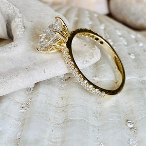 Pode incluir: Um anel de noivado de ouro com um grande diamante claro de forma quadrada. O anel tem uma banda de pequenos diamantes.