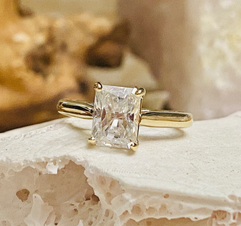 May include: A gold engagement ring featuring a large, clear, square-shaped diamond.