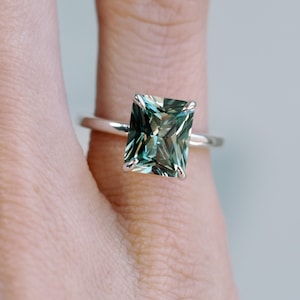 May include: A silver ring featuring a large, emerald-cut green gemstone.