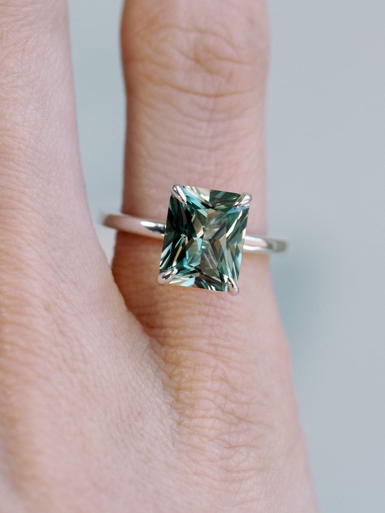 May include: A silver ring featuring a large, emerald-cut green gemstone.