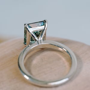 May include: A silver ring featuring a large, emerald-cut gemstone. The gemstone is a pale green colour with a hint of blue.