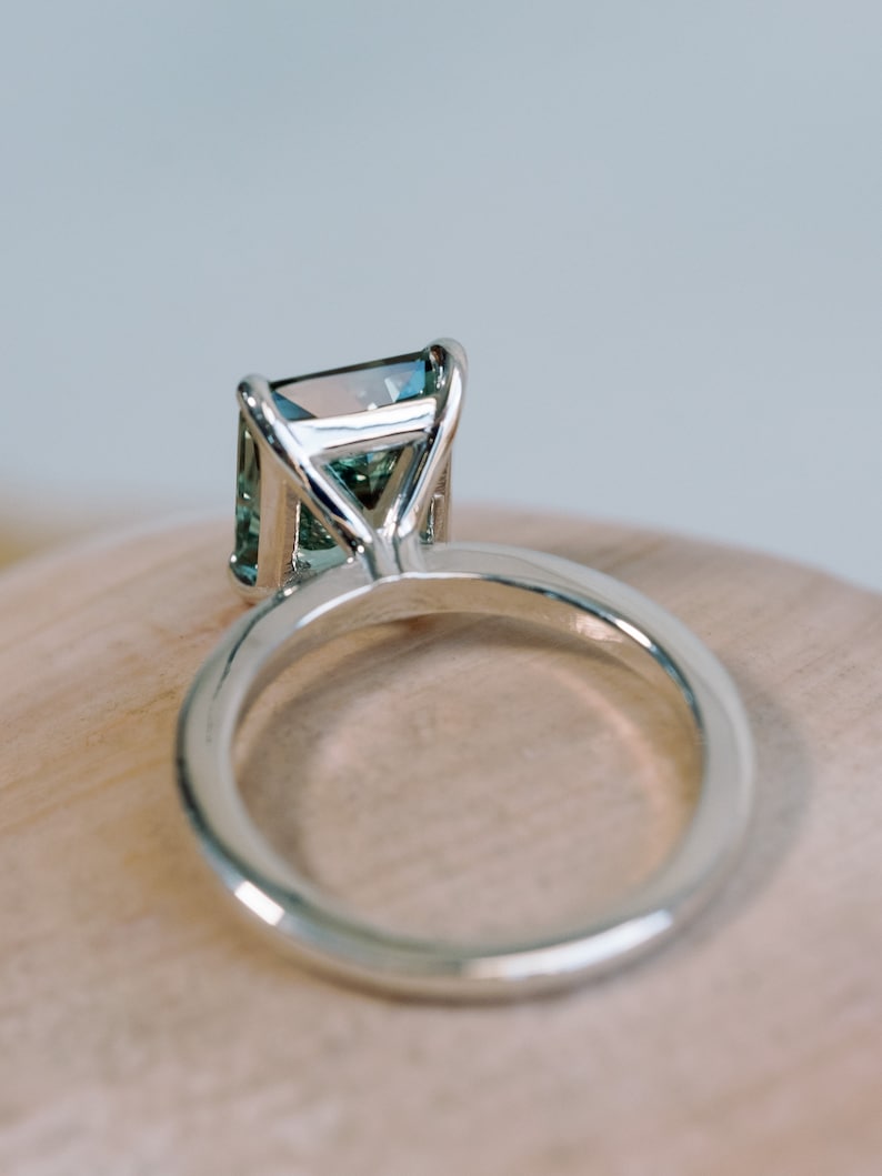 May include: A silver ring featuring a large, emerald-cut gemstone. The gemstone is a pale green colour with a hint of blue.