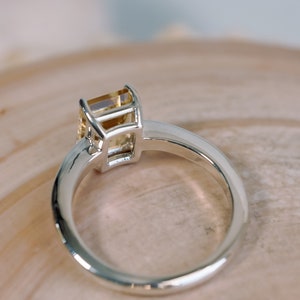 May include: A silver ring with a yellow gemstone set in a square bezel setting.