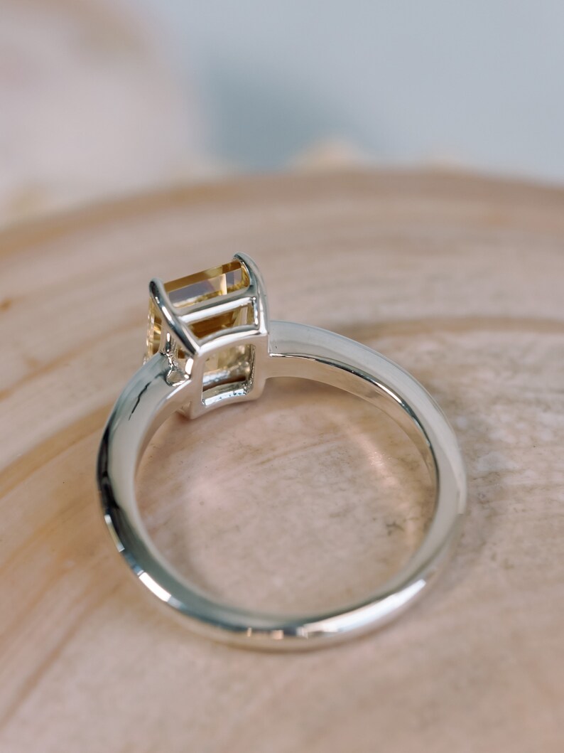 May include: A silver ring with a yellow gemstone set in a square bezel setting.