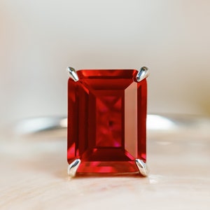 May include: A close-up of a ring with a large, emerald-cut ruby gemstone set in a silver band.