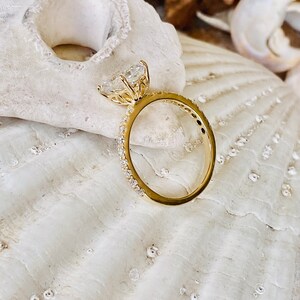Pode incluir: Um anel de noivado de ouro com um grande diamante de forma de cora&ccedil;&atilde;o claro engastado em garras. A banda &eacute; uma banda fina engastada em pav&eacute; com pequenos diamantes.