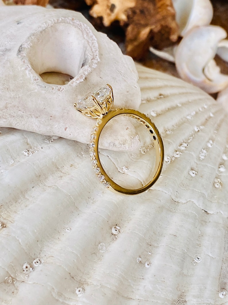 Pode incluir: Um anel de noivado de ouro com um grande diamante de forma de cora&ccedil;&atilde;o claro engastado em garras. A banda &eacute; uma banda fina engastada em pav&eacute; com pequenos diamantes.