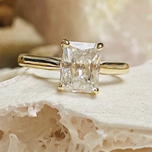 May include: A gold engagement ring featuring a large, clear, square-shaped diamond.