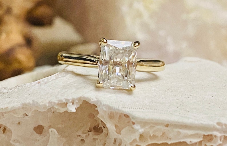 May include: A gold engagement ring featuring a large, clear, square-shaped diamond.