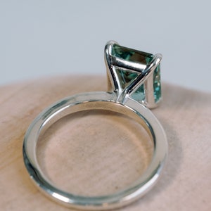 May include: A silver ring with a green gemstone set in a prong setting.