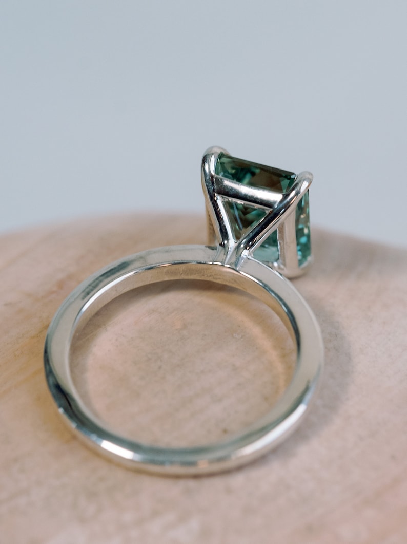 May include: A silver ring with a green gemstone set in a prong setting.