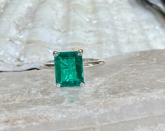 May include: A silver ring with a large emerald green gemstone set in a square shape.