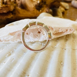 May include: A silver ring with a unique, geometric design. The ring is made of multiple small, rectangular pieces that are joined together to form a continuous band. The ring is shown on a white seashell background.