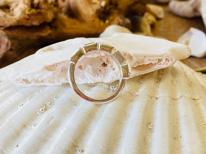 May include: A silver ring with a unique, geometric design. The ring is made of multiple small, rectangular pieces that are joined together to form a continuous band. The ring is shown on a white seashell background.