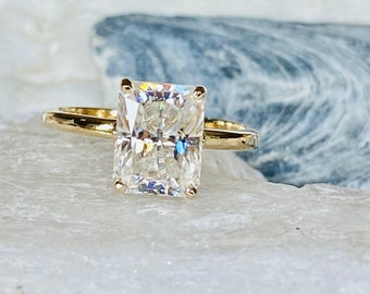 May include: A gold engagement ring with a large, clear, square-shaped diamond.