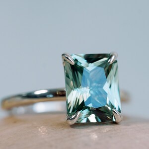 May include: A ring featuring a large, emerald-cut green gemstone set in a silver band.