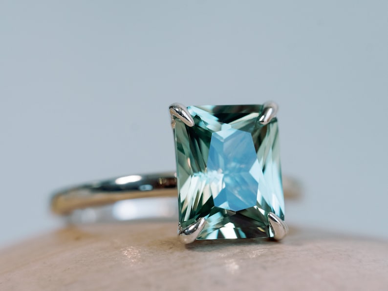 May include: A ring featuring a large, emerald-cut green gemstone set in a silver band.