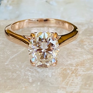 May include: A rose gold engagement ring with a large, round, clear diamond.